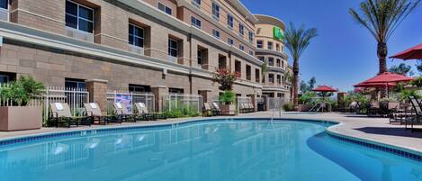 A hotel with a swimming pool, multiple floors, and outdoor seating areas.