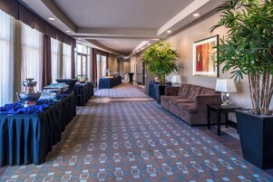 Un pasillo de hotel con alfombra estampada, un mostrador de recepción, un sofá y una planta grande en maceta.