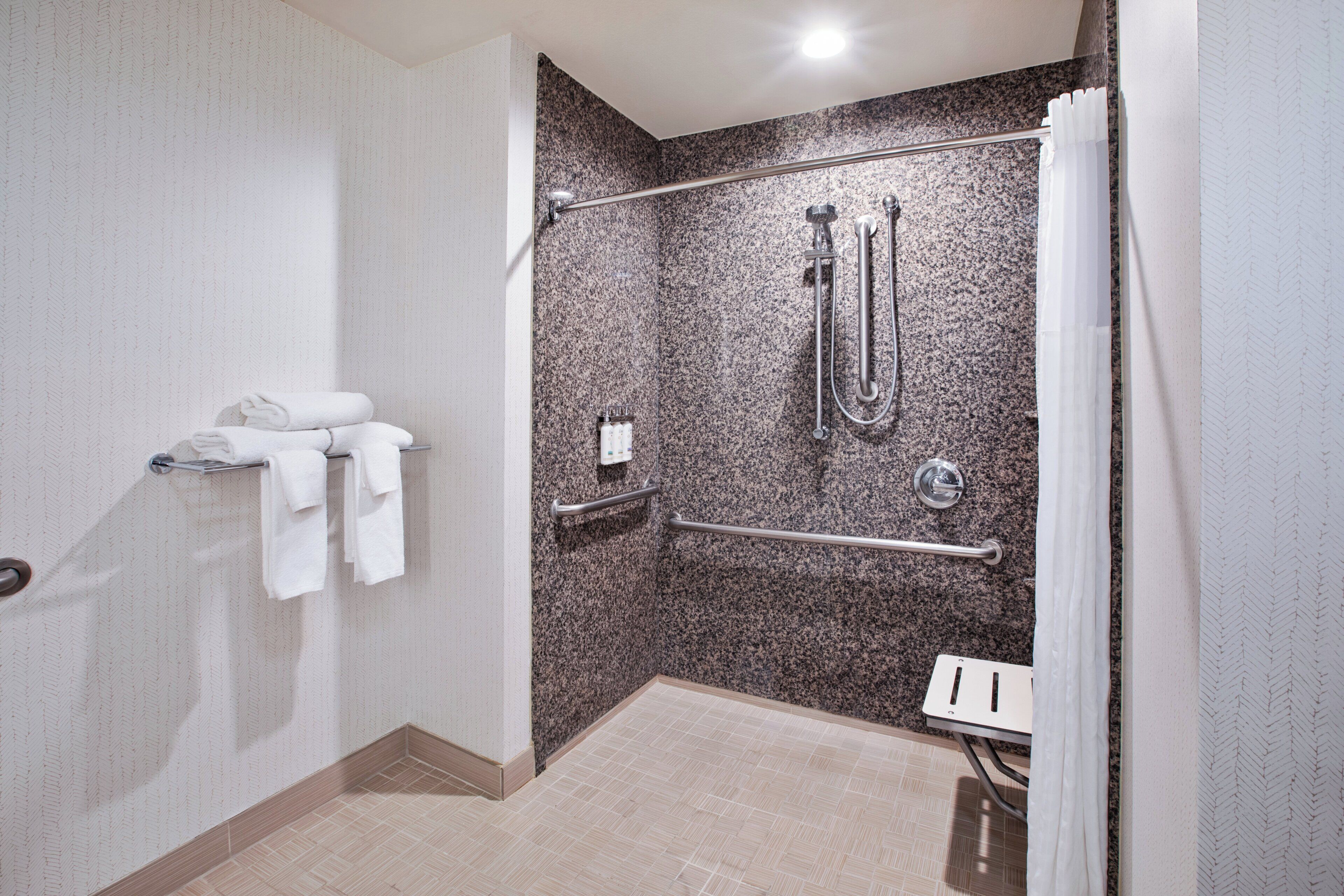 A modern bathroom with a shower, grab bars, and a towel rack.