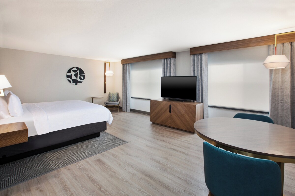 A hotel room with a bed, a TV, a dining table, and a chair.