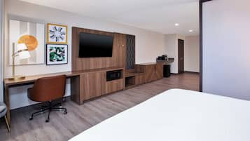 Een moderne hotelkamer met een houten bureau, een flatscreen televisie, een bed en kunst aan de muur.