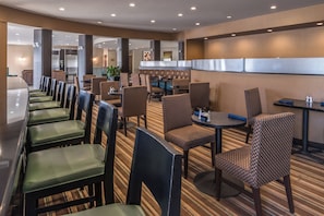 A hotel lobby with a long counter, seating area with patterned chairs, and a striped carpet. - Holiday Inn Ontario Airport by IHG (Ontario)