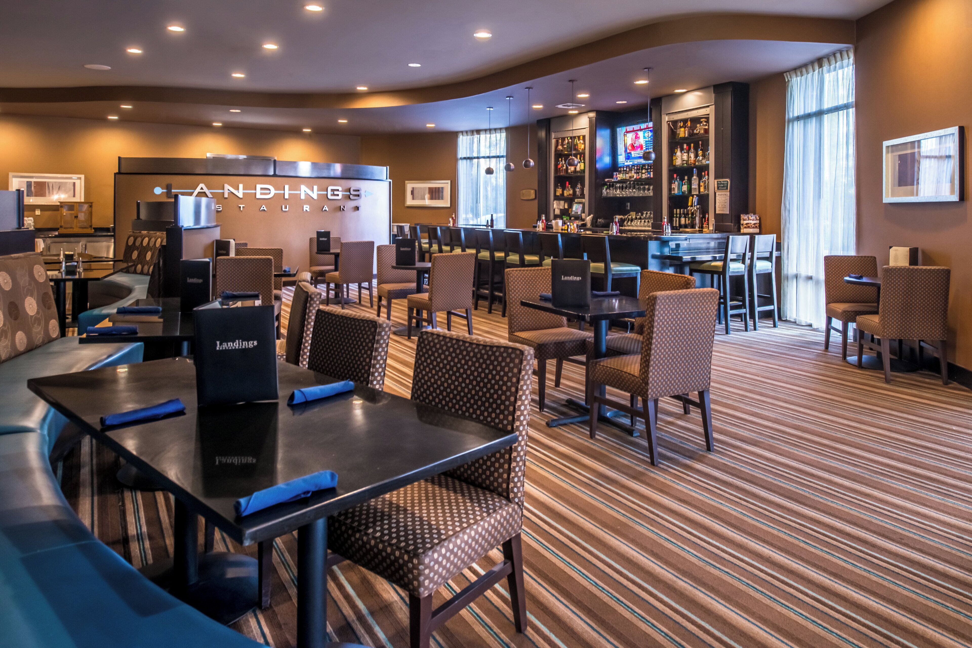 A hotel restaurant with multiple seating areas, a bar, and a television screen.