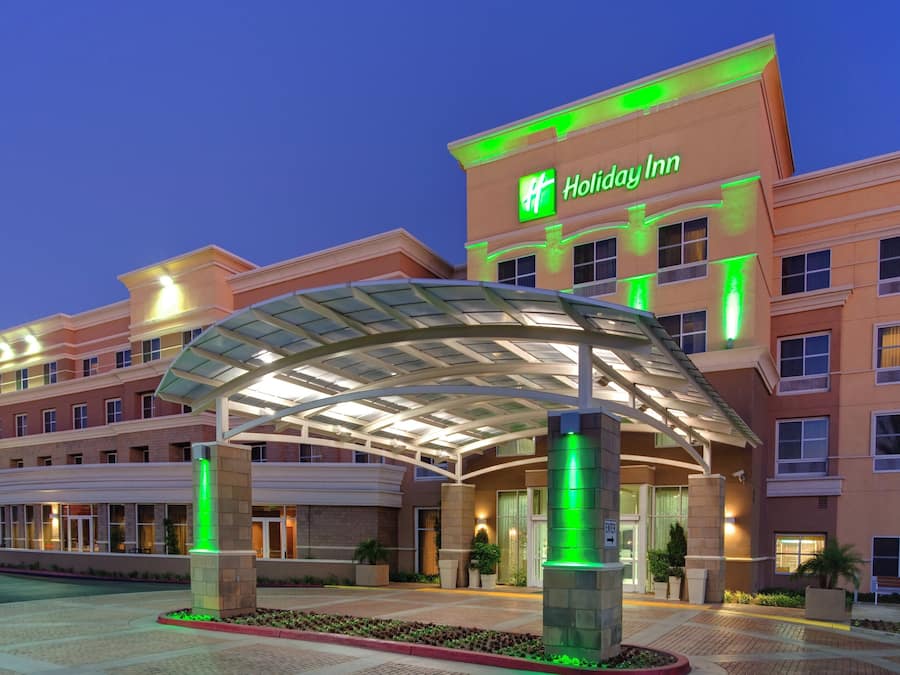Ein Holiday Inn Hotel mit überdachter Eingangspartei und einer begrünten Fläche davor.