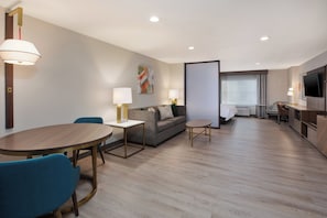 A modern hotel room with a dining area, a sofa, a TV, and a large window. - Holiday Inn Ontario Airport by IHG (Ontario)