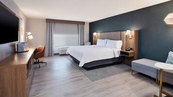 A modern hotel room with a large bed, a desk, a chair, a small table, and a TV.
