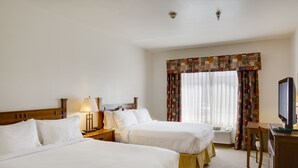 A hotel room with two beds, a television, a desk, and a window with curtains.