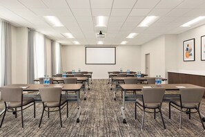 A conference room with tables, chairs, a projector screen, and water bottles. - Garner Hotel Houston Westchase by IHG (Houston)