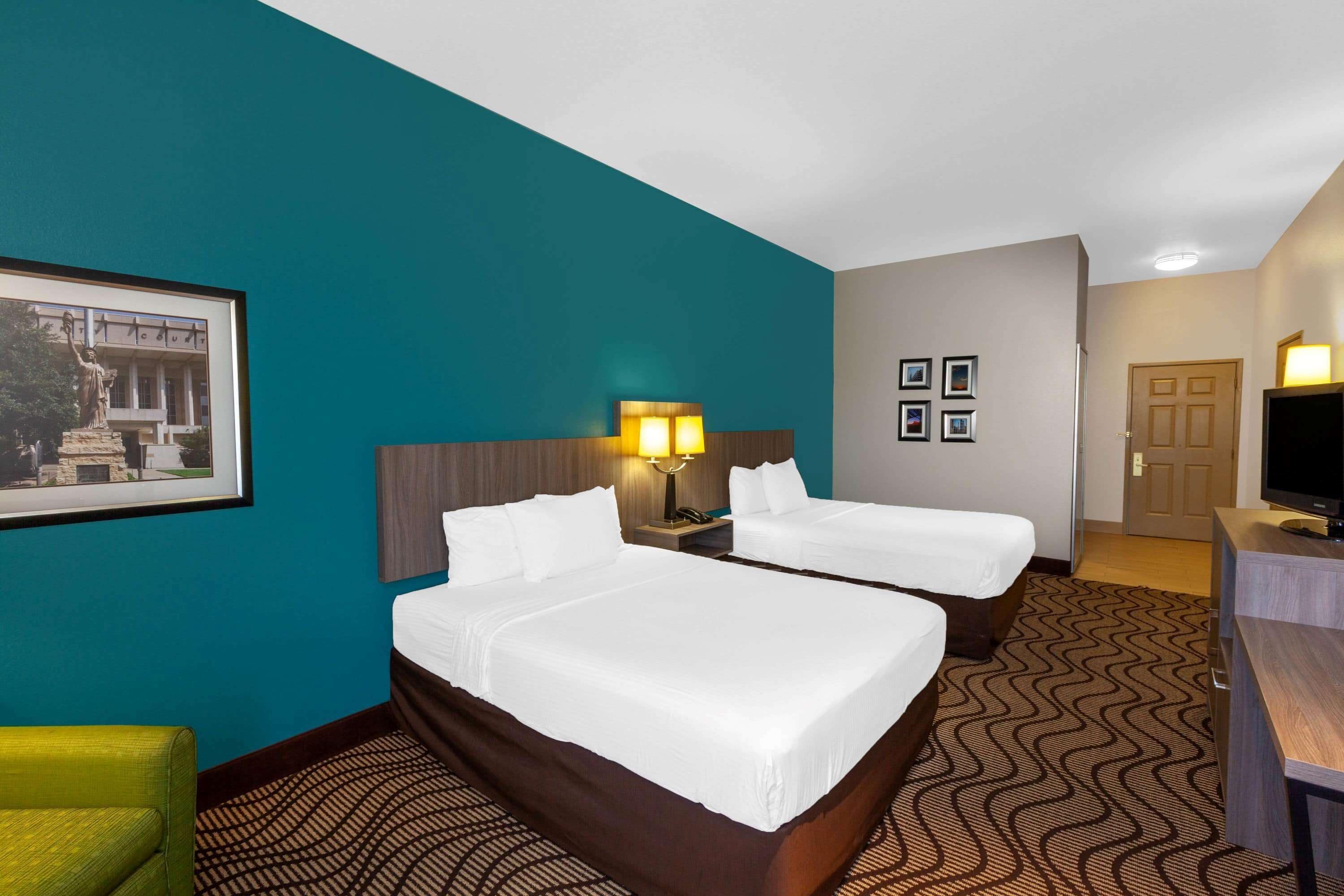 A hotel room with two beds, a desk, a television, and a framed picture on the wall.