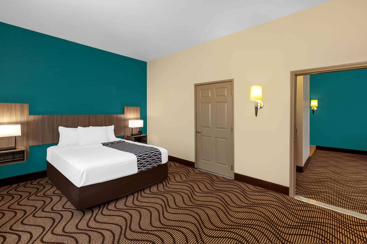 Ein Hotelzimmer mit einem Bett, zwei Nachttischlampen, einer Tür und einem Spiegel.