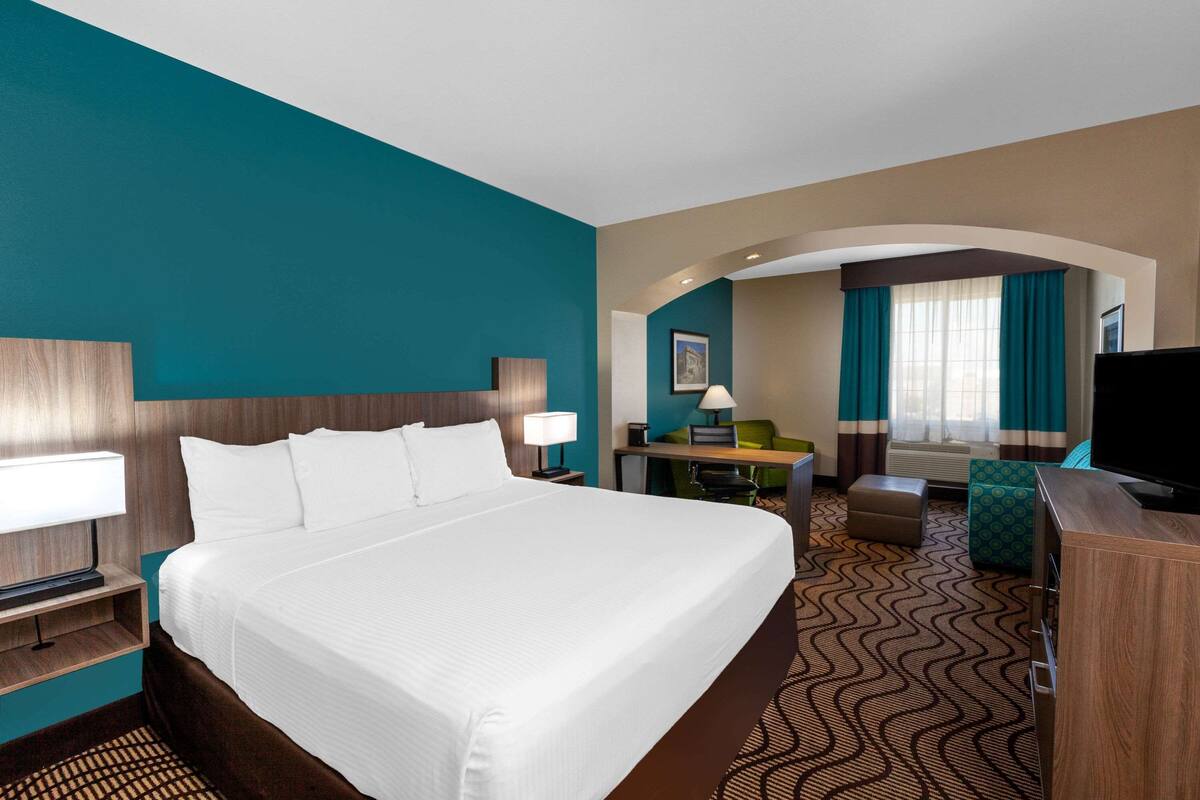 Ein Hotelzimmer mit einem großen Bett, einem Schreibtisch, einem Fernseher und einer Sitzecke mit Blick auf die Stadt.
