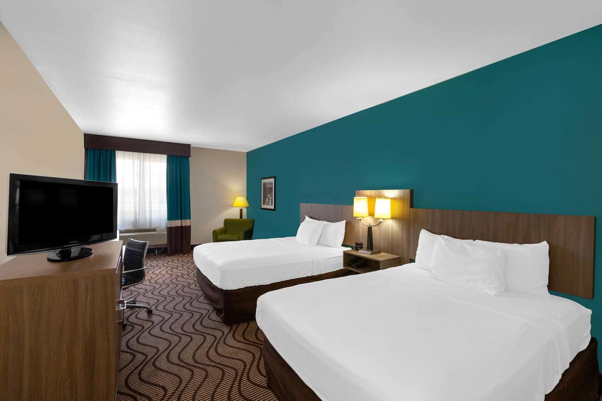 Ein Hotelzimmer mit zwei Betten, einem Schreibtisch mit Fernseher, einem Sessel und einer Schreibtischlampe.