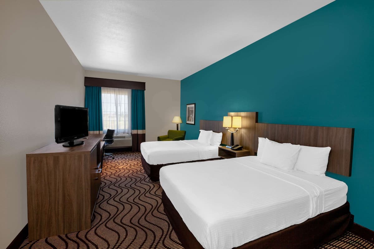Ein Hotelzimmer mit zwei Betten, einem Schreibtisch, einem Fernseher, einer Schreibtischlampe und einem Stuhl.