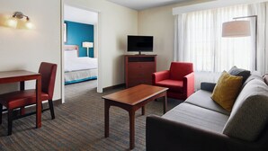 A hotel room with a bed, a TV, a red chair, a sofa, and a wooden table. - Residence Inn by Marriott Killeen (Killeen)