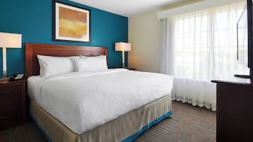 A hotel room with a large bed, two bedside tables, a nightstand, a desk, and a window with sheer curtains.