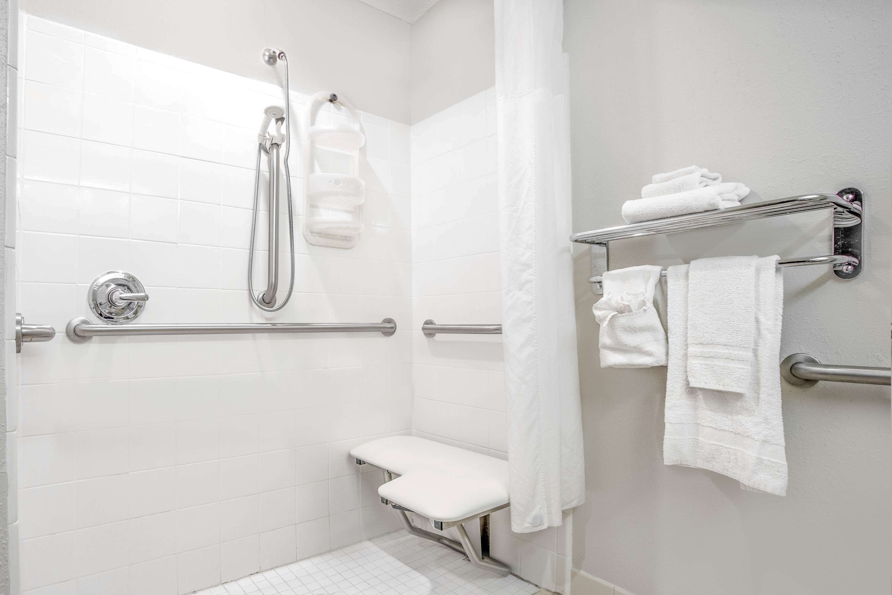 Un baño moderno con azulejos blancos, una ducha con cabezal de ducha manual, un banco y toalleros.