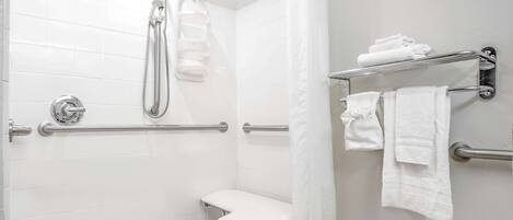 Un baño moderno con azulejos blancos, una ducha con cabezal de ducha manual, un banco y toalleros.