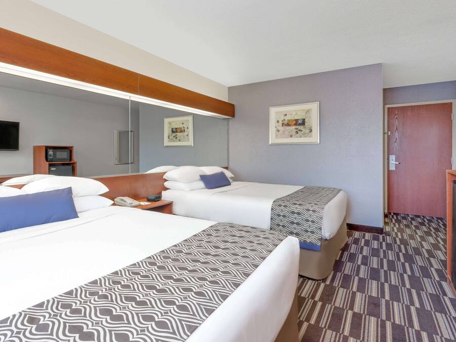 Una habitación de hotel con dos camas, cabecera de madera, televisor de pantalla plana, microondas y una mesita.