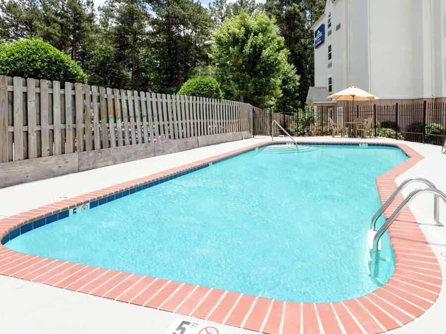 A rectangular pool with a brick edge, surrounded by a wooden fence and a building in the background.