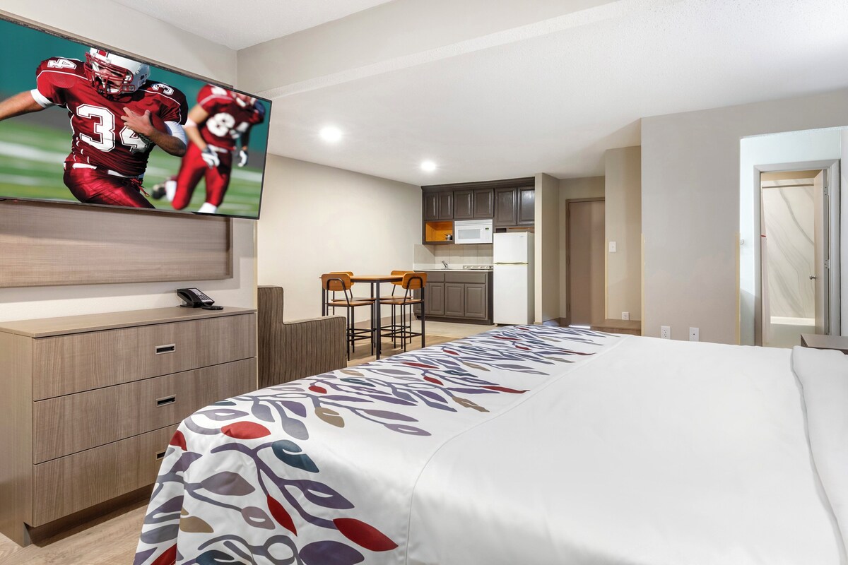 Ein Hotelzimmer mit Bett, Schreibtisch, Fernseher, Küchenzeile und Essecke.