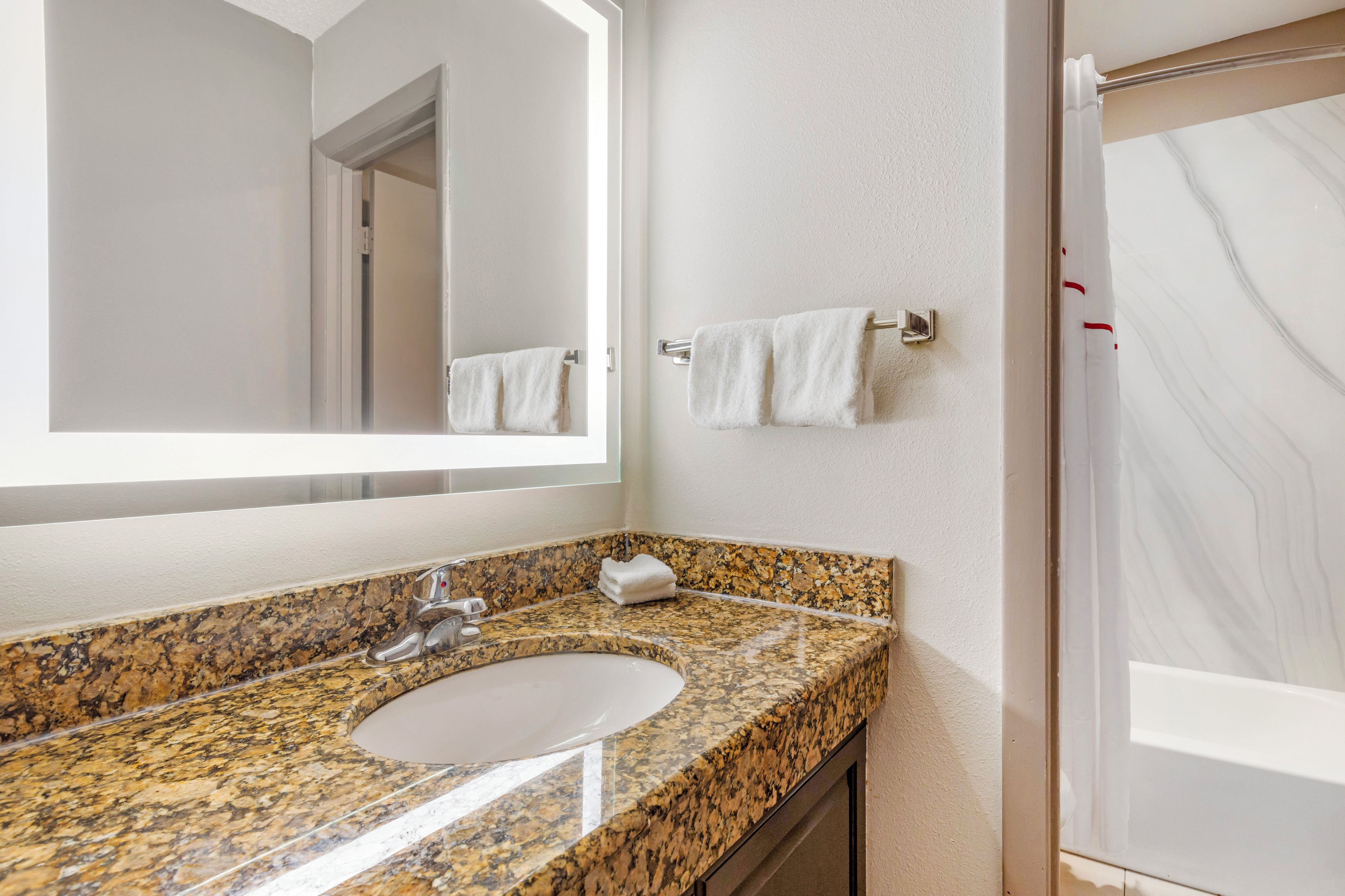 Une salle de bain avec un lavabo doté d’un plan de travail en granit, un miroir, un porte-serviettes et un espace douche.