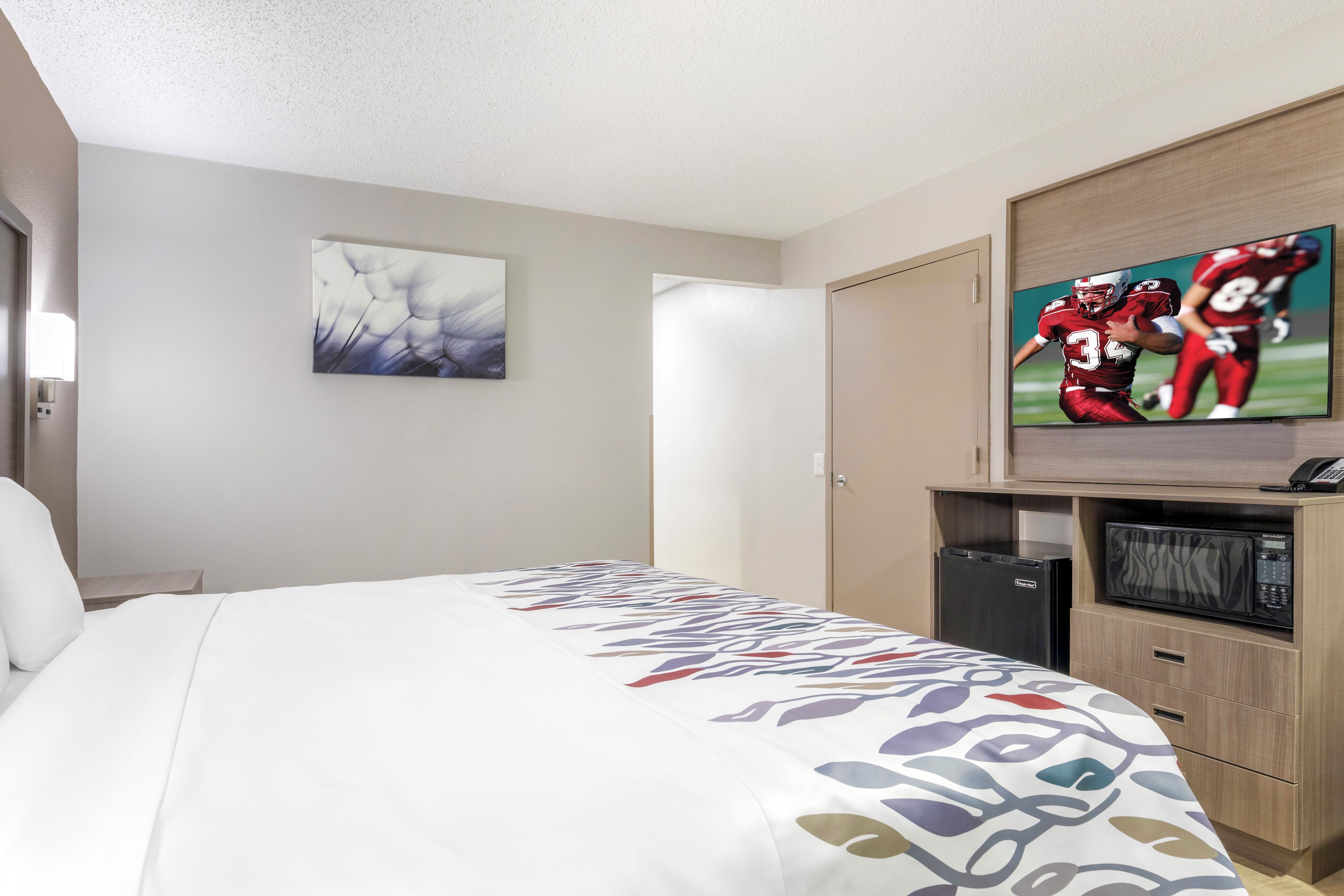 Una habitación de hotel con una cama, un televisor mostrando un partido de fútbol, un refrigerador y un microondas.