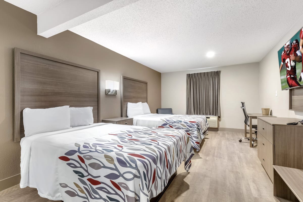 Habitación de hotel con dos camas, un escritorio, una silla, un televisor y una ventana con cortinas.
