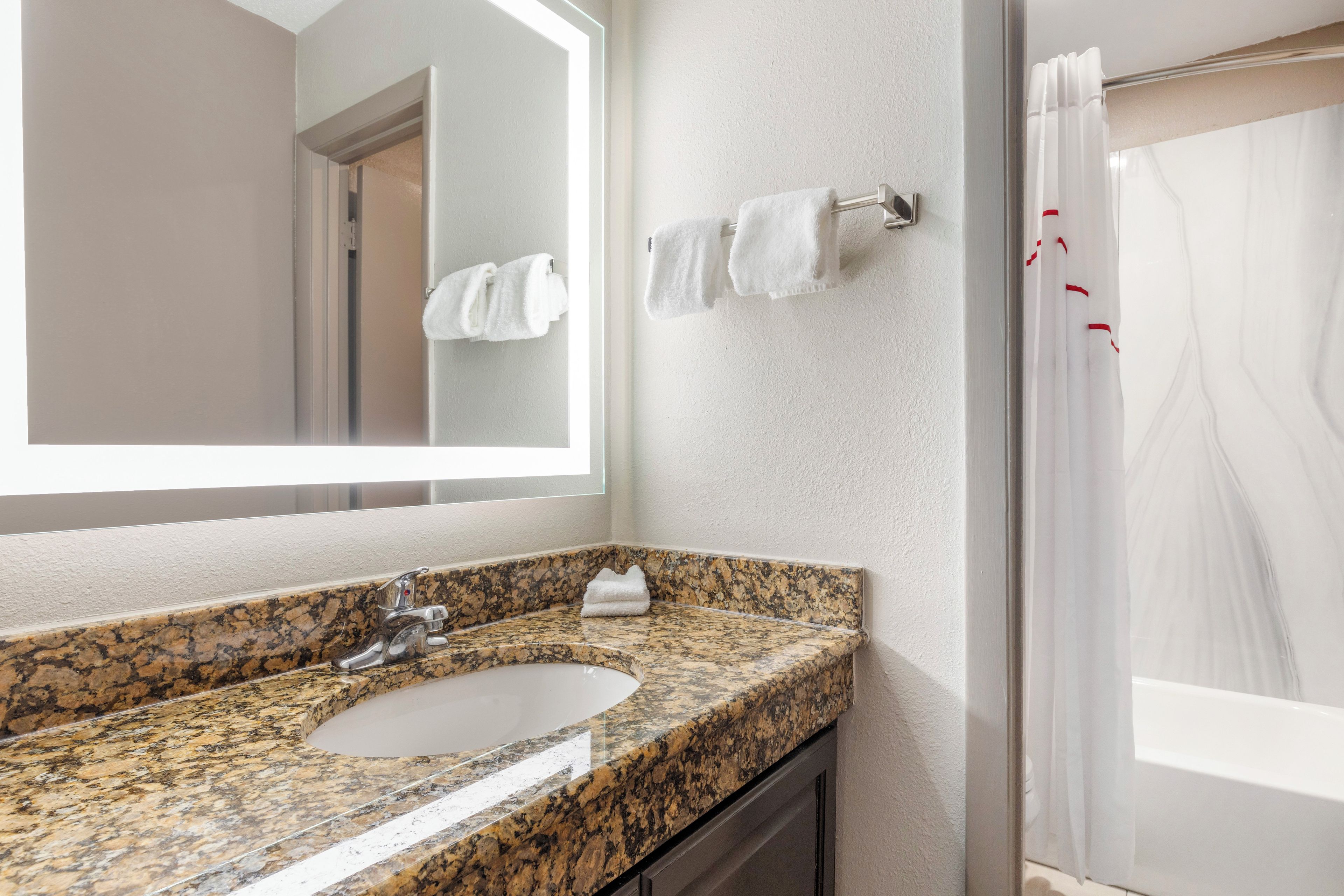 A bathroom with a granite countertop sink, a mirror, a towel rack, and a shower curtain.
