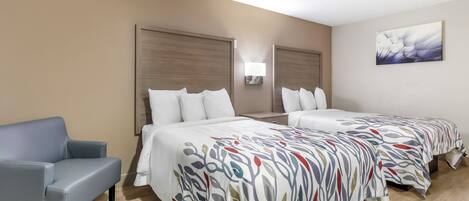 A hotel room with two beds, a sofa, and a wall-mounted light fixture.