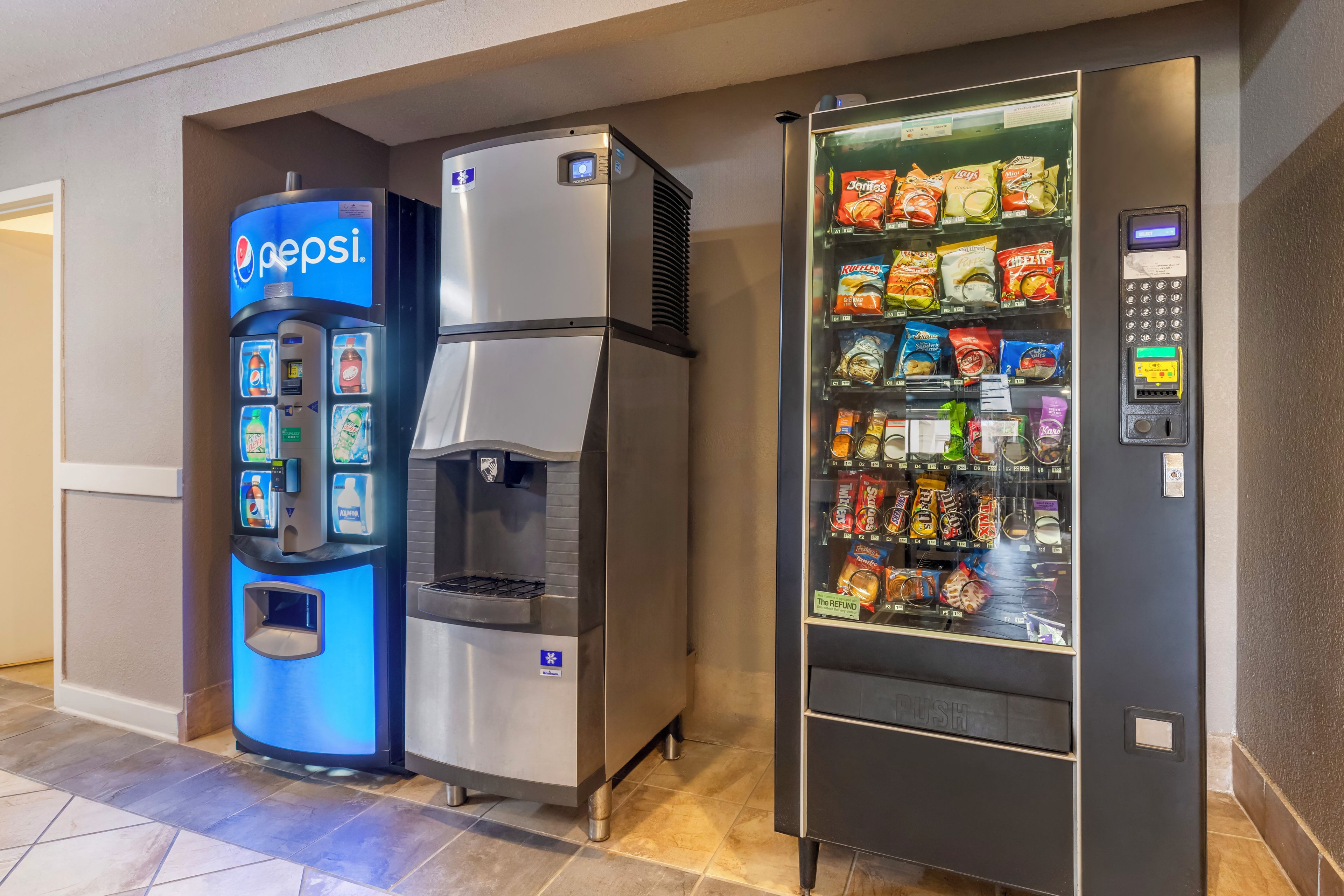 Een automaat met een Pepsi logo, een waterdispenser en een snackautomaat met diverse merken.