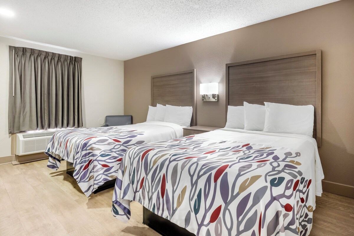A hotel room with two beds, a flat-screen TV, and a large window with curtains.