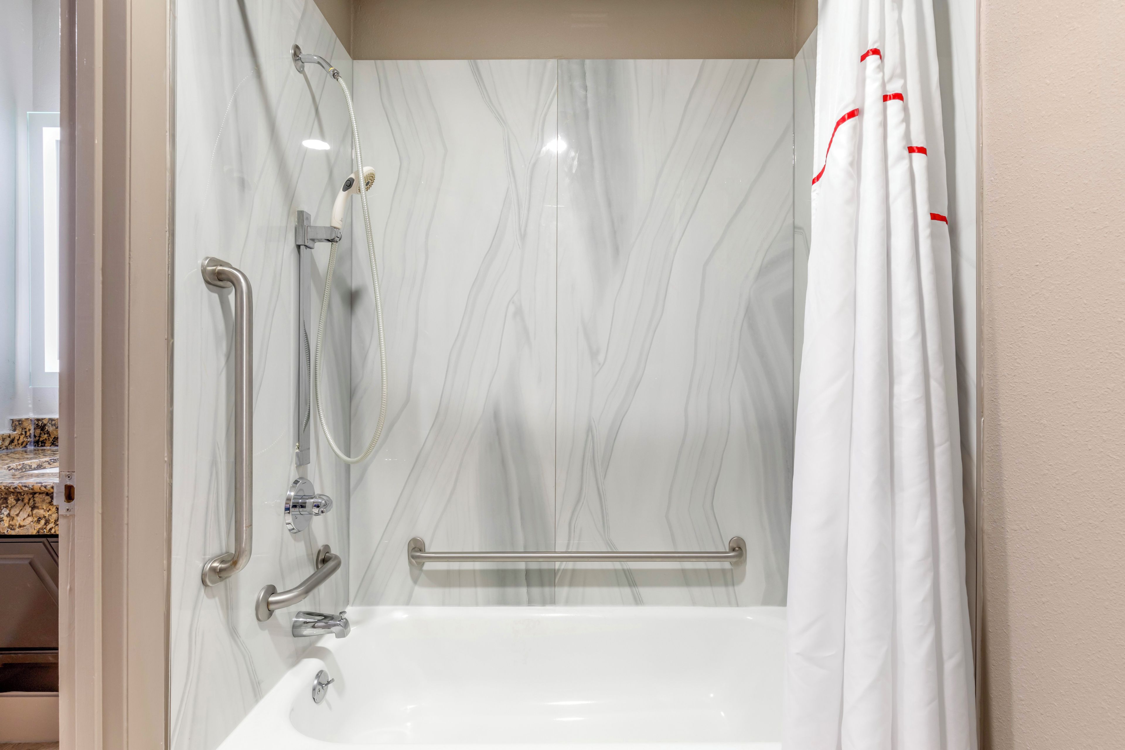 Ein Badezimmer mit einer weißen Badewanne, einer Dusche inklusive Duschbrause und einer Haltestange.