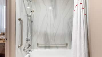 Ein Badezimmer mit einer weißen Badewanne, einer Dusche inklusive Duschbrause und einer Haltestange.
