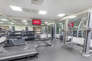 Ein Fitnessstudio mit unterschiedlichen Trainingsgeräten, darunter Laufbänder und Kraftgeräte, sowie ein Schild, das kostenloses WLAN anzeigt.