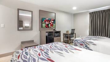 Une chambre d’hôtel avec deux lits, un téléviseur fixé au mur, un bureau avec une chaise et une fenêtre avec des rideaux.