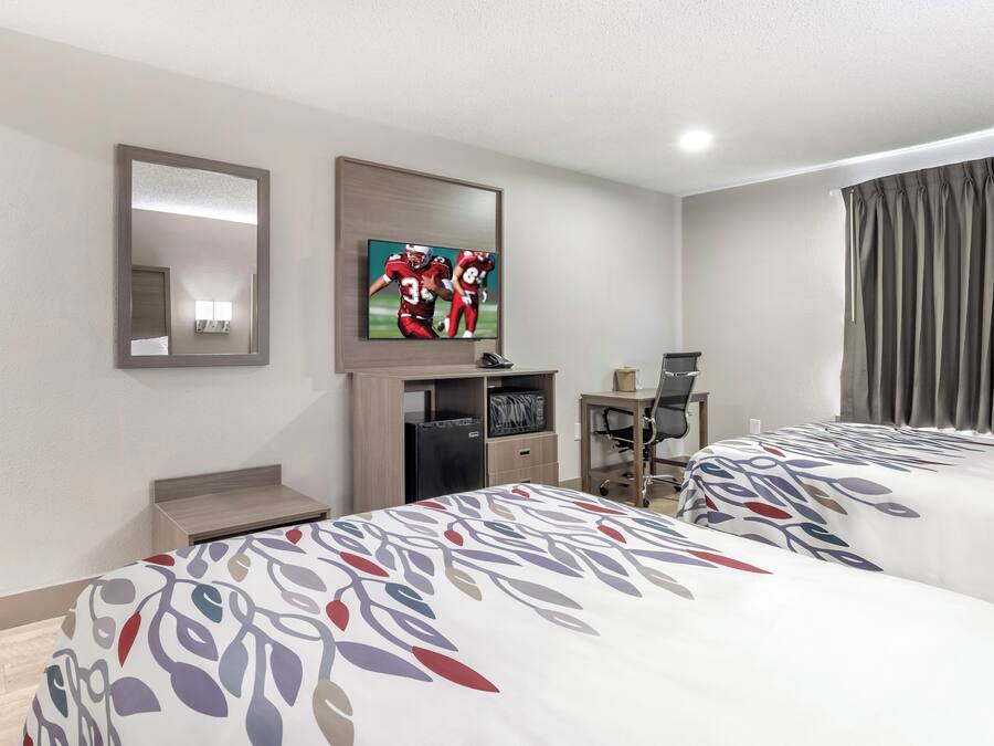 Une chambre d’hôtel avec deux lits, un téléviseur fixé au mur, un bureau avec une chaise et une fenêtre avec des rideaux.
