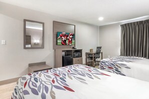 Een hotelkamer met twee bedden, een aan de muur bevestigde televisie, een bureau met een stoel en een raam met gordijnen.