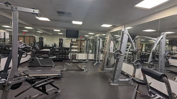 Un gimnasio con diversos equipos de ejercicio, incluyendo cintas de correr, máquinas de pesas y pesas libres.