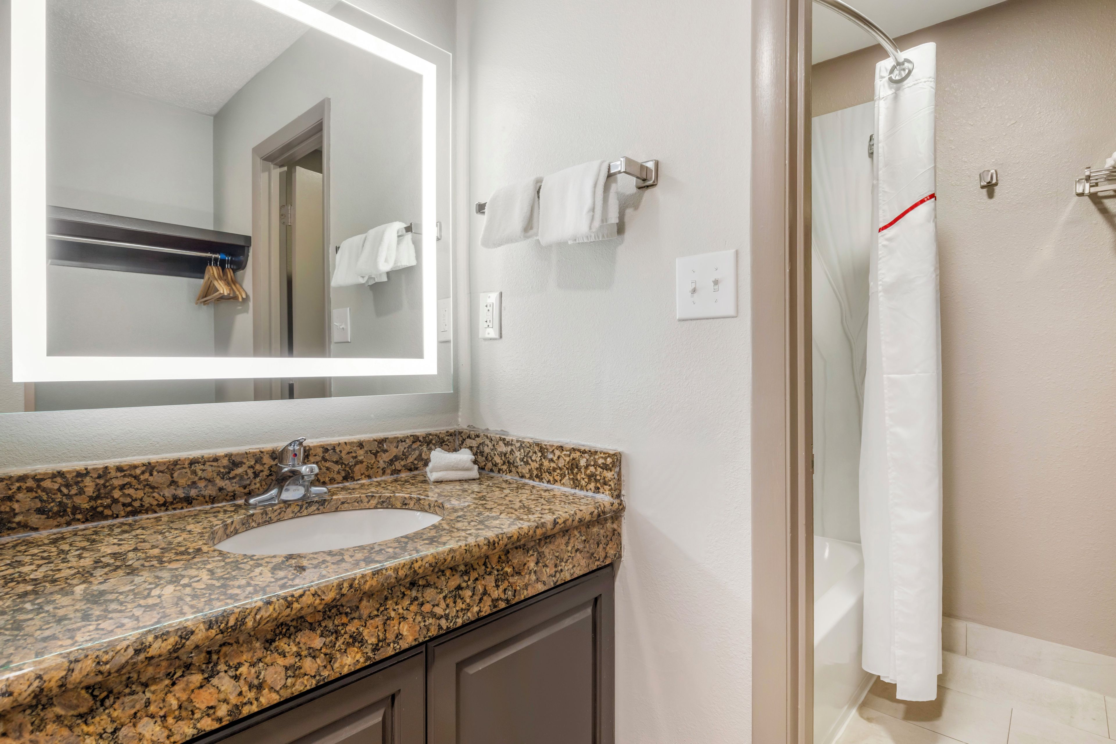 A bathroom with a granite countertop sink, a mirror, a shower curtain, and a towel rack.