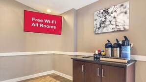 Un hall d’hôtel avec un panneau indiquant que le Wi-Fi est gratuit dans toutes les chambres, un coin café avec des bouilloires et une œuvre d’art accrochée au mur.