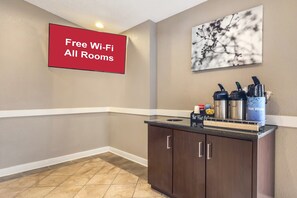 Eine Hotelhalle mit einem Schild, das „Kostenloses WLAN in allen Zimmern“ anzeigt, einer Kaffeestation mit verschiedenen Getränken und einem an der Wand hängenden Kunstwerk.