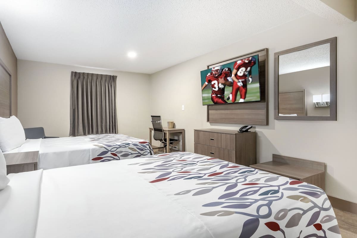 Habitación de hotel con dos camas, televisión, escritorio y espejo.