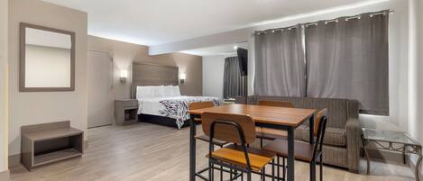A hotel room with a bed, a desk with chairs, a sofa, a TV, and a window with curtains.