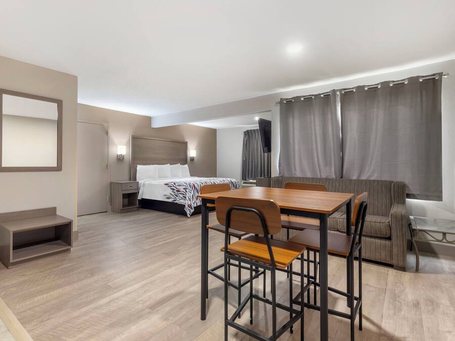 A hotel room with a bed, a desk with chairs, a sofa, a TV, and a window with curtains.