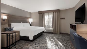 A hotel room with a bed, bedside tables, a desk, a chair, a television, and a window with curtains.