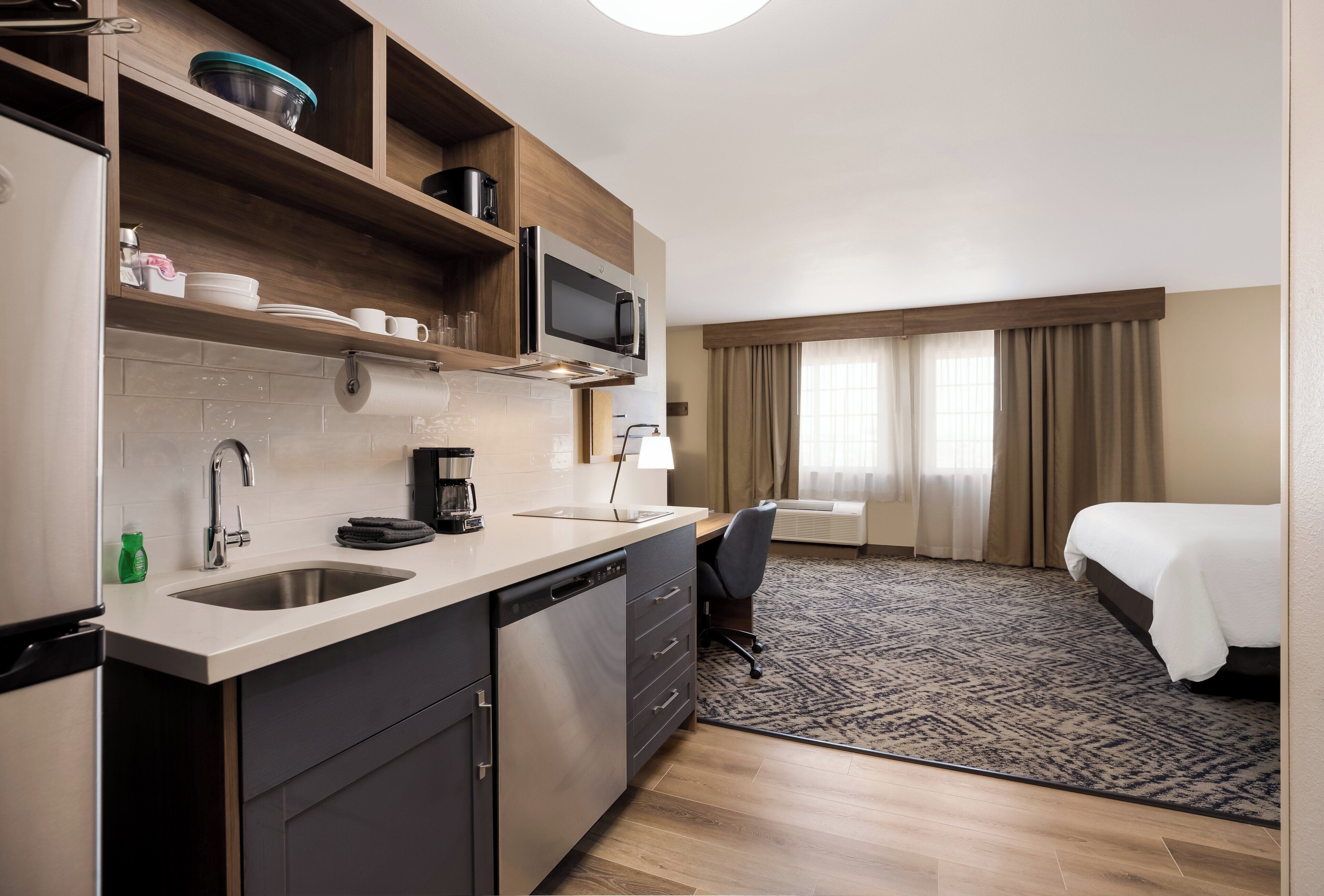 Ett hotellrum med ett litet kök, en säng, ett skrivbord och ett fönster med gardiner.