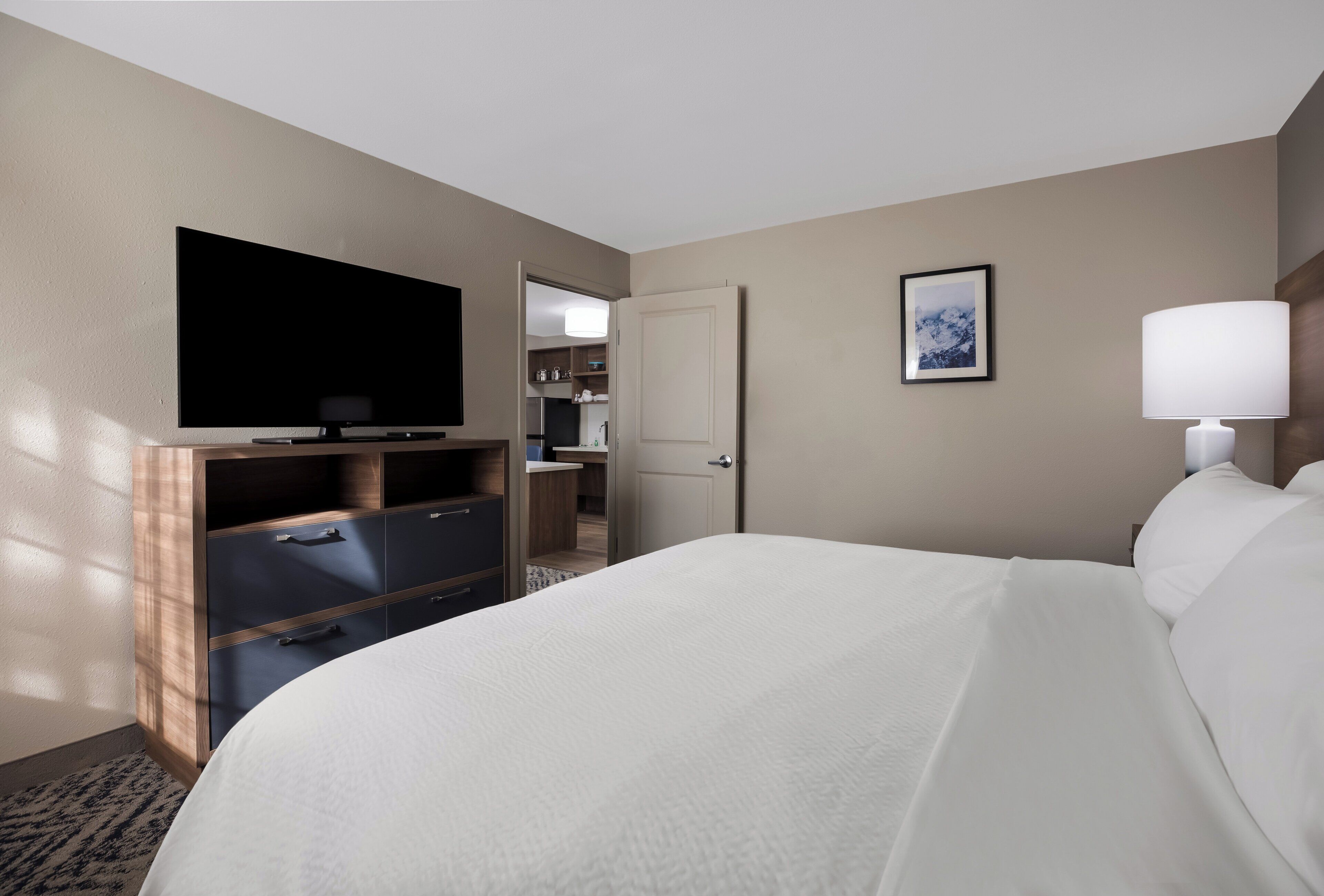 A hotel room with a bed, a TV, a desk, a wardrobe, a door, and a picture on the wall.