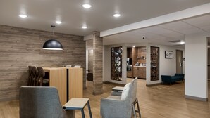 A modern reception area with a wooden wall, a black pendant light, and a seating area with two grey chairs and a small table.