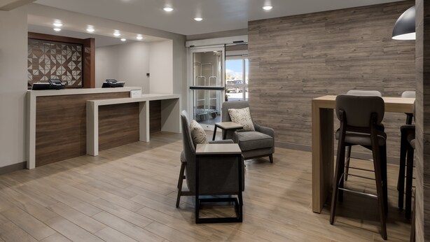 A modern reception area with a wooden reception desk, seating area with chairs and a table, and a glass door leading outside.