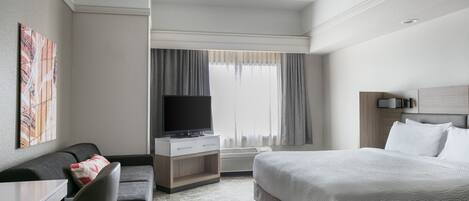 Una camera d'albergo con un letto, una scrivania con una sedia, una televisione e una finestra con tende.